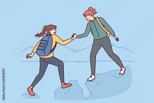 Woman on hike helps female friends by climbing peak of high cliff and shaking new apex. Hiking trip of two young girls with backpacks traveling through dangerous high mountain areas