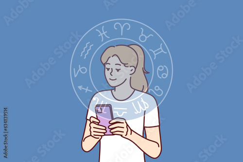 Woman reads astrological horoscope forecast on phone or finds out compatibility with zodiac signs. Horoscope wheel near girl with smartphone using mobile application with aracul predicting future