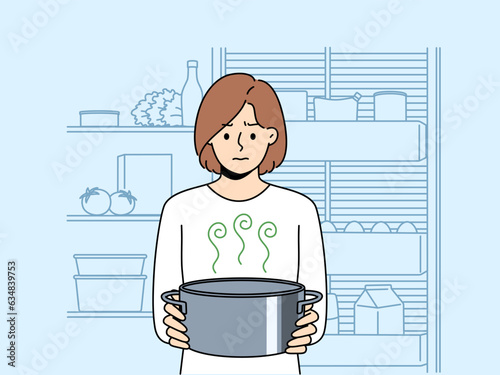 Frustrated woman housewife with pot of sour soup, feels bad smell from food spoiled due to violation of sanitary rules. Girl is standing in kitchen and holding stinking soup in bewilderment