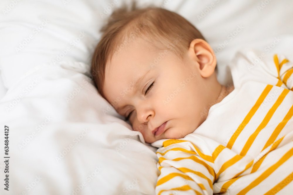 Little baby girl sleeping peacefully on bed and grimacing, resting during daytime sleep with eyes closed, copy space Little baby girl sleeping peacefully on bed and grimacing, resting during daytime sleep with eyes closed, copy space