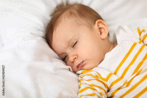 Little baby girl sleeping peacefully on bed and grimacing, resting during daytime sleep with eyes closed, copy space