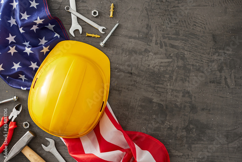 Celebrate the crucial role of construction workers on American Labor Day. Top view shot of american flag, worker equipment, safety helmet on concrete grey background with empty space for promo or text