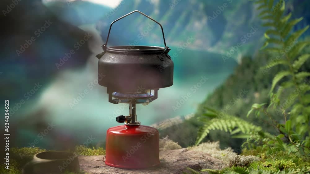 Cooking, making coffee or tea on a portable camping gas burner with a red gas cylinder with scandinavian nature background. Summer hiking, ecotourism, survival. Cooking, making coffee or tea on a portable camping gas burner with a red gas cylinder with scandinavian nature background. Summer hiking, ecotourism, survival.