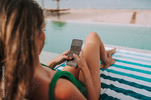 Chica joven delgada en cama balinesa y tumbona leyendo y escribiendo con el smartphone photo