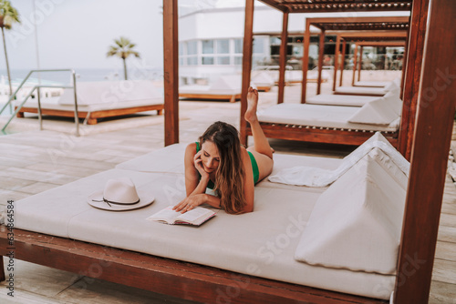 Chica joven delgada en cama balinesa descansando y leyendo tranquilamente  photo