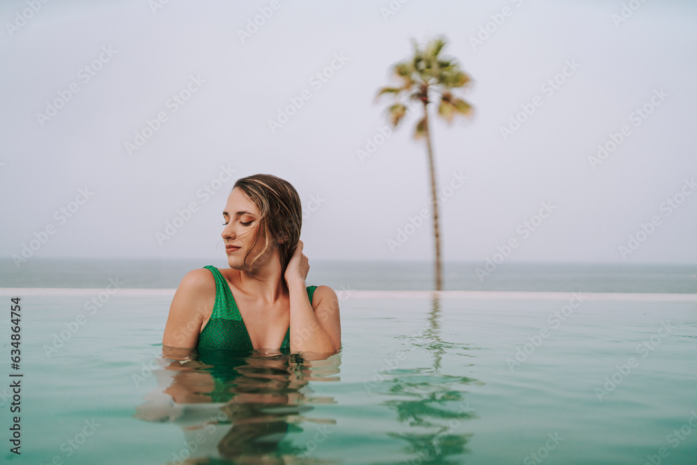Chica delgada con pelo largo posando en una piscina de un hotel paradisiaco 