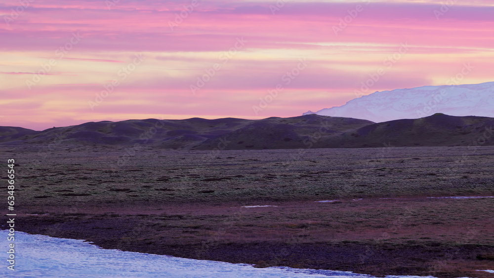 Beautiful pink sky in icelandic scenery with hills and snowy mountains, scandinavian nordic fields on countryside scenic route. Majestic skies and nature in iceland. Handheld shot.