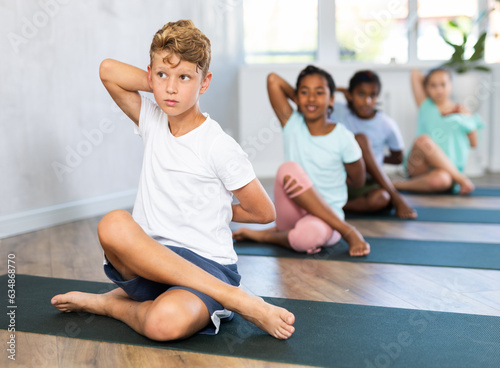 Children doing gomukhasana sitting on rug on floor. Concept of straightening of spine and toning of the abdominal organs.