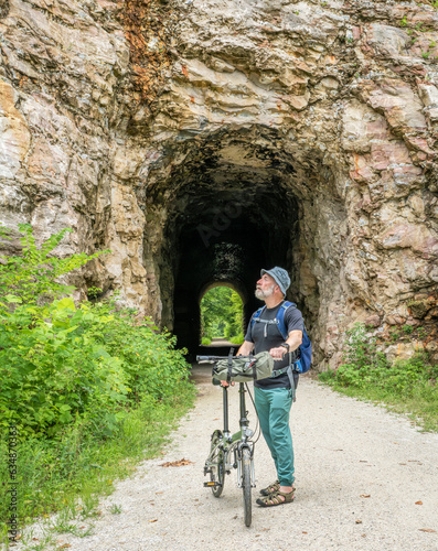 Senior man with a folding bike on Katy Trail at a tunnel near Rocheport, Missouri, summer scenery. The Katy Trail is 237 mile bike trail converted from an old railroad. photo
