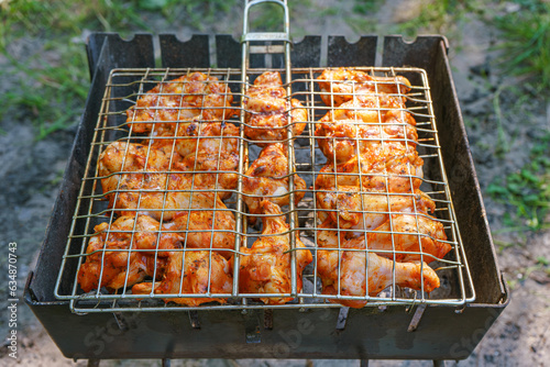 Spicy marinated chicken wings and legs on grill and on a summer barbecue. Cooking process on flame in braizer outside. BBQ, picnic, street food. photo