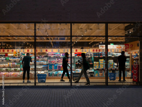 A look through a window in a supermarket at night. People go shopping.