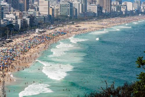 Leblon and Ipanema beach in Rio de Janeiro, Brazil. Sunny day with blue sky and many people on the beach. Plenty of umbrellas on the sand. Weekend. Turquoise and clear sea photo