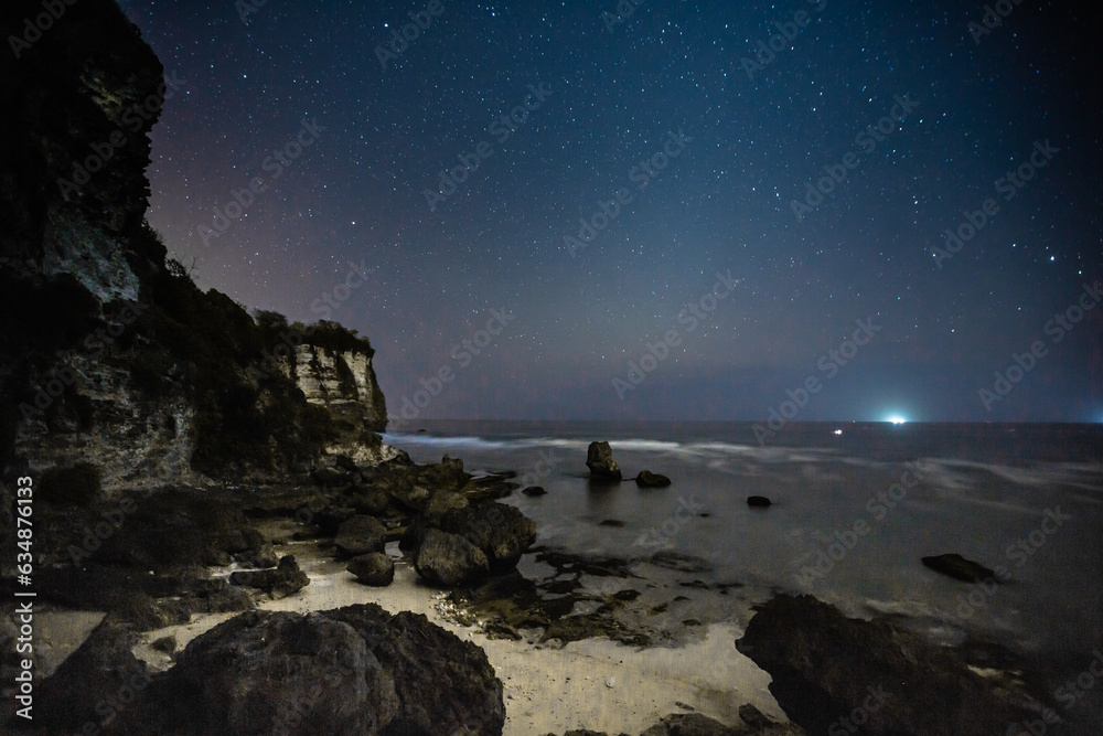 To the left, a towering cliff looms, grounded in the embrace of the sea. To the right, the vast expanse of a star-speckled sky stretches endlessly, painting a celestial contrast by the waterside. To the left, a towering cliff looms, grounded in the embrace of the sea. To the right, the vast expanse of a star-speckled sky stretches endlessly, painting a celestial contrast by the waterside.