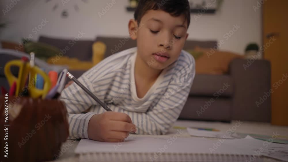 Latin boy focused on homework painting in notebook in living room. Children on the carpet at home drawing in their free time. Concept of entertainment and kid development. Latin boy focused on homework painting in notebook in living room. Children on the carpet at home drawing in their free time. Concept of entertainment and kid development.
