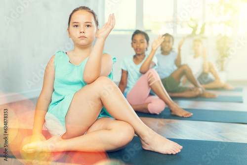 Happy preteen children exercising yoga in pose Gomukhasana in fitness center