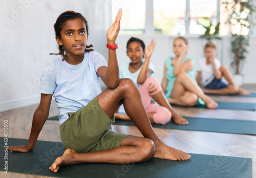 Group of children practicing yoga in the fitness studio, posing in pose Gomukhasana