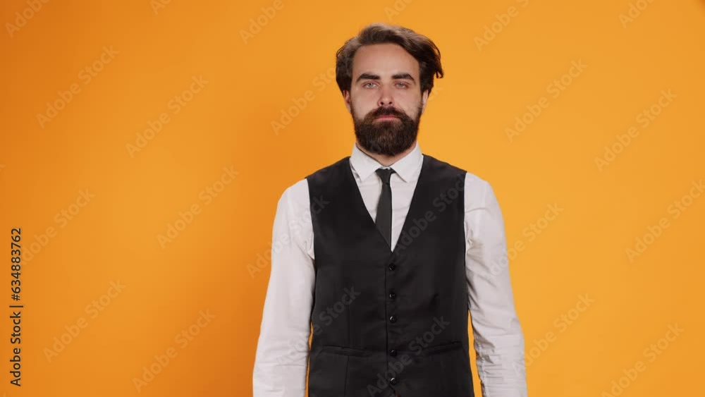 Staff member gives thumbs down on camera, showing negative dislike sign against yellow background. Man restaurant employee expressing disagreement with bad gesture, displeased butler. Staff member gives thumbs down on camera, showing negative dislike sign against yellow background. Man restaurant employee expressing disagreement with bad gesture, displeased butler.