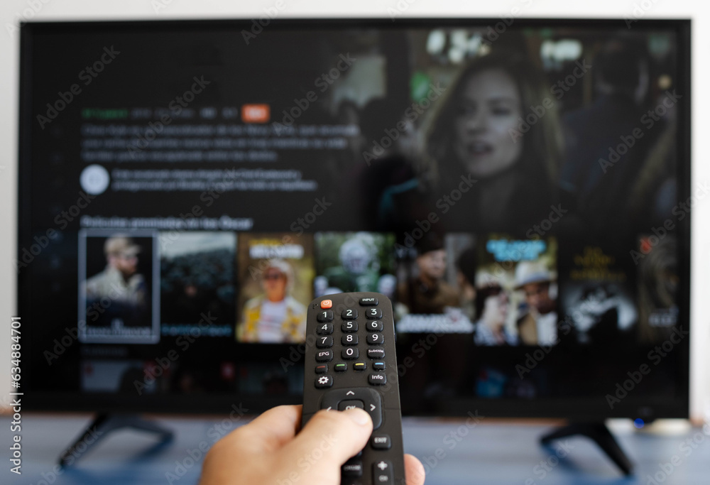 Fototapeta premium Hand holding a remote control while putting a serie on television