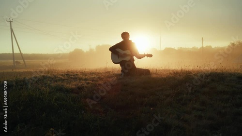 Artistic man singing song playing acoustic guitar outdoor at cinematic misty fog sunset sunrise countryside field. Charismatic art male play musical instrument live performance melody musician star 4k