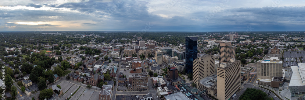 Drone panorama of the skyline of Lexington, Kentucky, displays the financial business district in the foreground and the University of Kentucky campus in the distance, set against a cloudy sunrise.