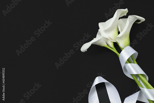 Beautiful calla lilies and white ribbon on black background, flat lay with space for text. Funeral symbol photo