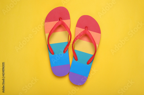 Rainbow flip flops on yellow background, flat lay. LGBT pride