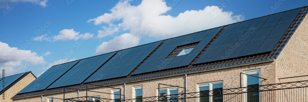 Fototapeta premium Newly build houses with solar panels attached on the roof against a sunny sky , Close up of new building with black solar panels in the Netherlands