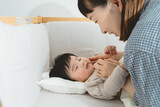 春の日中、ベビーベッドで横たわり女性にほっぺを触れられるアジア人の黒髪の赤ちゃん