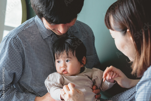 秋の昼間、部屋で父親に抱っこされ母親と手を繋ぎあやされるアジア人の赤ちゃん photo