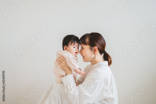 Obraz w ramie 春の日中、屋内の壁の前で赤ちゃんを抱っこして見つめる立つアジア人の女性