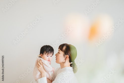 Foto 春の日中、室内の壁の前で小さい子どもを抱っこして見つめる日本人のママ