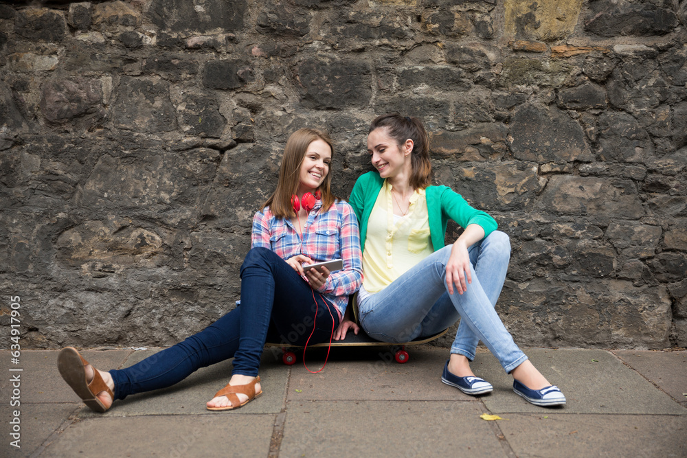 Two fashionable women sitting on skateboard.