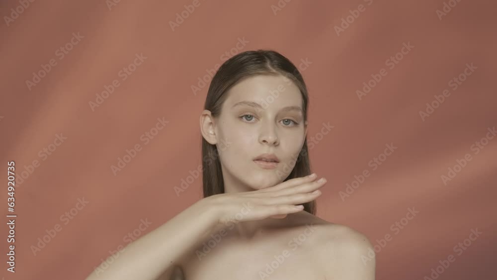A young seminude woman touches a clean, moisturized face in the studio on a red background. Facebuilding. The concept of natural beauty, plastic surgery, cosmetology, skin care. Slow motion. HDR