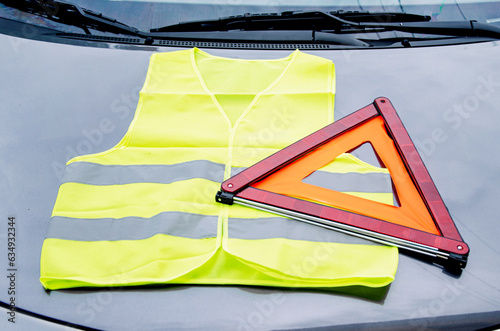 yellow reflective vest and warning triangle lie on hood of car. Safety on road in case of breakdown