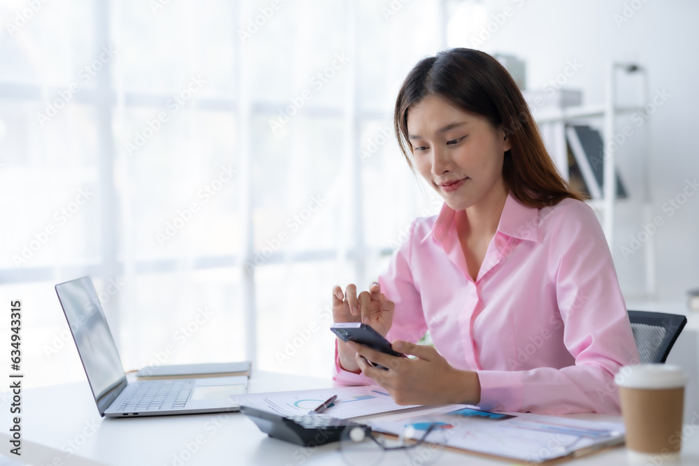Portrait of a smiling asian businesswoman using mobile phone in the office. Young Asian businesswoman with paperwork at workplace using smartphone in a modern office. Portrait of a smiling asian businesswoman using mobile phone in the office. Young Asian businesswoman with paperwork at workplace using smartphone in a modern office.