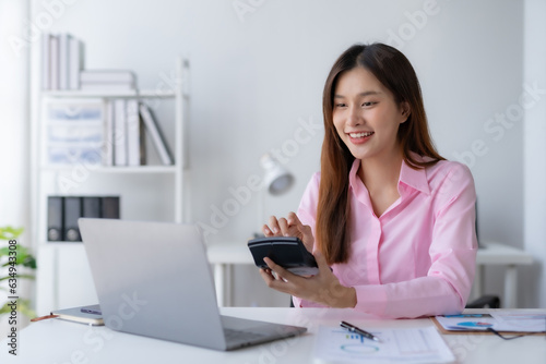 Young Asian businesswoman using a calculator to calculate business principles. Accounting statistics concept at the office.