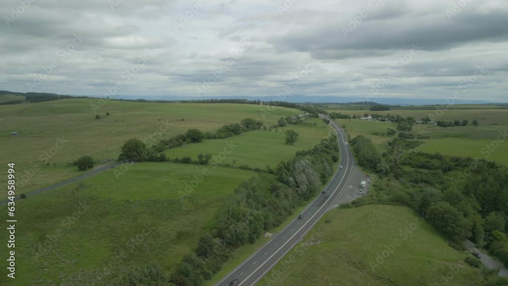 Orbit of busy rural road A66 showing green countryside with reveal of hill Great Mell Fell on cloudy summer day. English, Lake District, Cumbria, UK. Orbit of busy rural road A66 showing green countryside with reveal of hill Great Mell Fell on cloudy summer day. English, Lake District, Cumbria, UK.