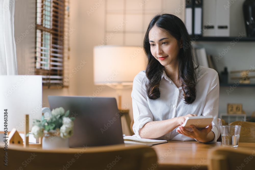 A millennial Asian businesswoman is sitting and working with laptop computer in her home kitchen, while also enjoying a relaxing cup of coffee. A millennial Asian businesswoman is sitting and working with laptop computer in her home kitchen, while also enjoying a relaxing cup of coffee.