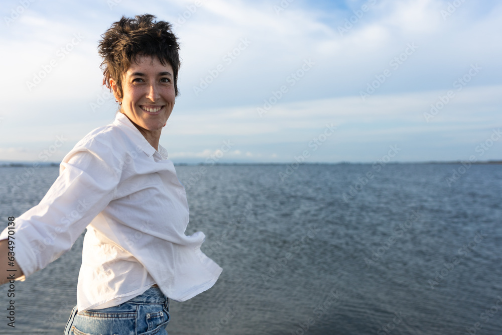 short-haired woman smiling on the beach, wearing white shirt, red top and denim, blue sky and calm sea. short-haired woman smiling on the beach, wearing white shirt, red top and denim, blue sky and calm sea.