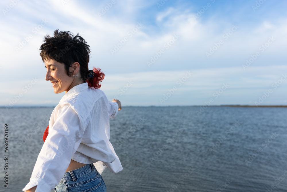 short-haired woman smiling on the beach, wearing white shirt, red top and denim, blue sky and calm sea. short-haired woman smiling on the beach, wearing white shirt, red top and denim, blue sky and calm sea.
