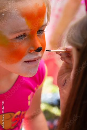 The face of a girl painted with colorful paints. Painting children's faces during a family picnic.