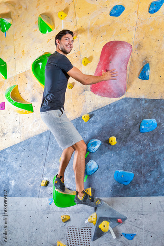 Professional Male Rock climber man hanging on a bouldering climbing wall, inside on colored hooks.