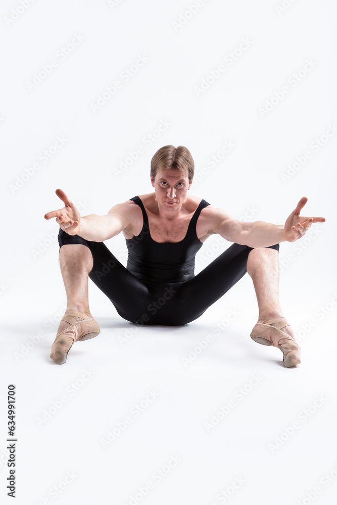 Obraz premium Ballerino Dancer Sitting While Practising Legs and Arms Forward Stretching Exercices Before Training In Black Sportive Tights in Studio.