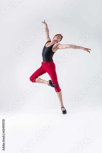 Fototapeta Naklejka Na Ścianę i Meble -  Ballet Ideas. Contemporary Ballet of Flexible Athletic Man Posing in Red Tights in Dance Pose With Hands Lifted on One Feet in Studio on White.