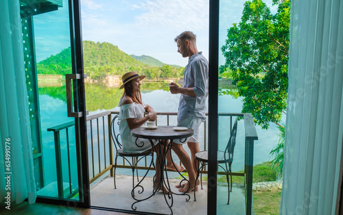 couple on vacation in Thailand drinking coffee in the morning on their balcony looking out over a lake and mountains in central Thailand. 
