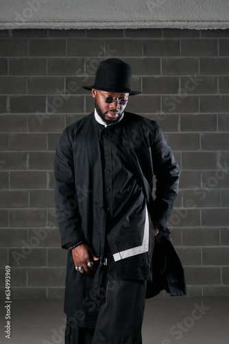 Stylish African American man in black outfit near brick wall