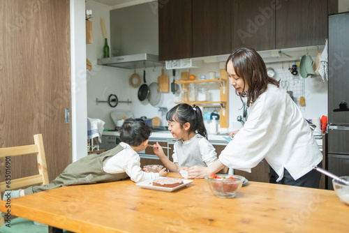 秋の日中に家の台所で集まってケーキ作りをする笑顔の日本人の母親と姉弟