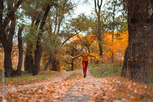 a young teenage girl runs through the autumn forest along a dirt road and enjoys the beautiful nature and bright yellow leaves