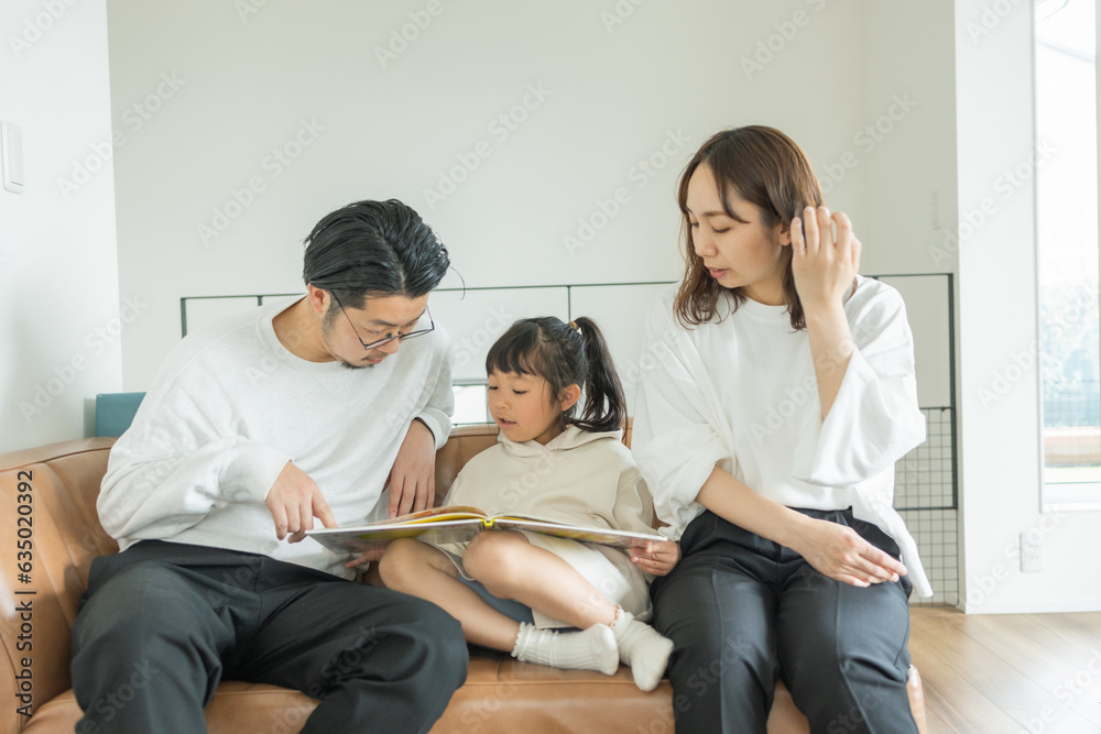春の日中、座って本を持ちながら親と会話する日本人の小学生の女の子 春の日中、座って本を持ちながら親と会話する日本人の小学生の女の子