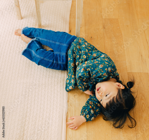 秋の午後、リビングの床の上で眠そうに寝転がる花柄の緑色のチュニックを着てデニムを履いたお団子ヘアの日本人の女の子 photo